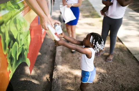 Girl reaching for meal from summer meals food truck