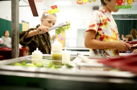 Boy holding tongs with lettuce in cafeteria line