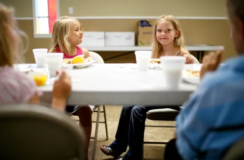 Two girls sitting at a fold out table eating and smiling