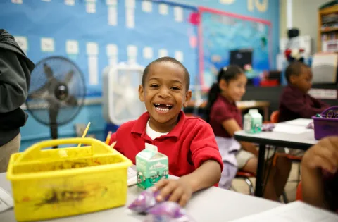 Boy smiling and eating breakfast at his classroom desk