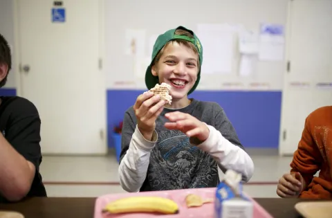 A smiling boy eats a sandwich at school.