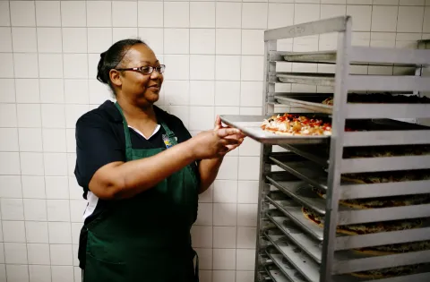 A cafeteria worker preparing trays of breakfast 