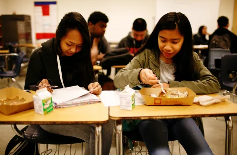 Two girls eating breakfast at their desks