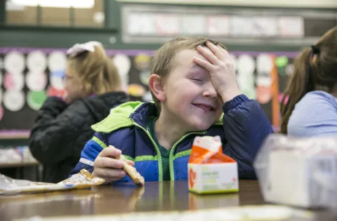 boy with hand on forehead eating breakfast in classroom