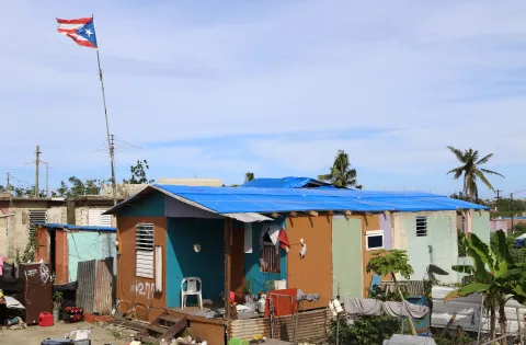 Home covered with blue tarp and Puerto Rican flag waving above it.