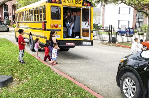 Families line up behind a school bus to receive meals that your donations helped support.