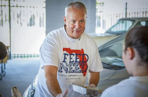 John Rivers serves meals while wearing a Feed the Need t-shirt and gloves.