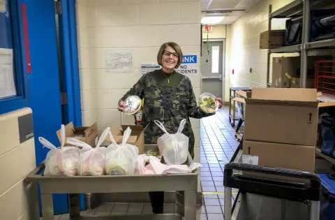 A woman holds up two donated, packaged salads behind a cart packed with meals for families need.