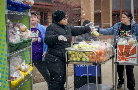 Three food service workers handle bags of fruit outside in the snow.