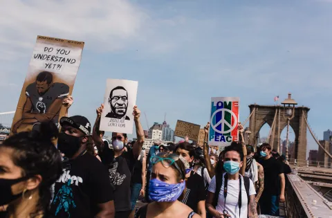 Racial justice protestors in coronavirus masks cross the Brooklyn bridge carrying signs remembering George Floyd.