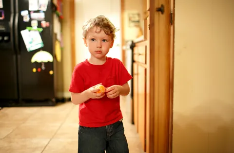 A little boy with a sad look on his face stands in his kitchen