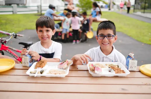 two kids eating a lunch outside