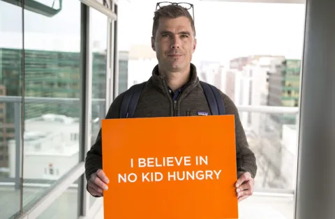 Chef holding sign that says I beleive in No Kid Hungry