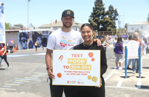 Ayesha and Stephen Curry hold a sign promoting our free meals texting service.