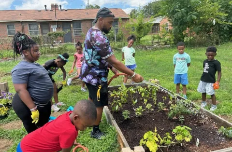 Young man watering garden surrounded by kids