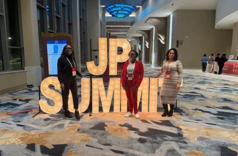 Three women in front of JP Summit Sign