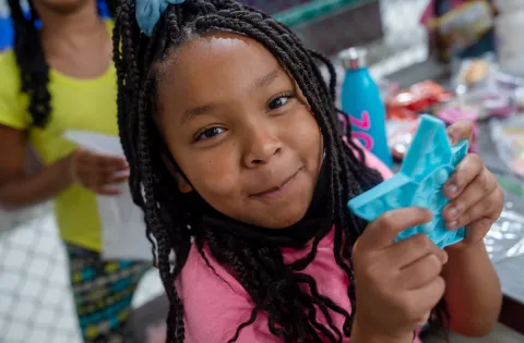Smiling young black girl in pink shirt holding blue plastic star.