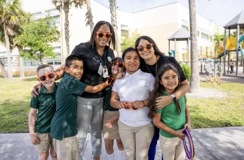5 elementary school students (2 boys on the left and 3 girls on the right) standing with their female teachers outside Gove Elementary School in Florida.