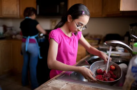 Girl washing strawberries in kitchen at home