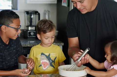 Kids in kitchen gathered around mixing bowl